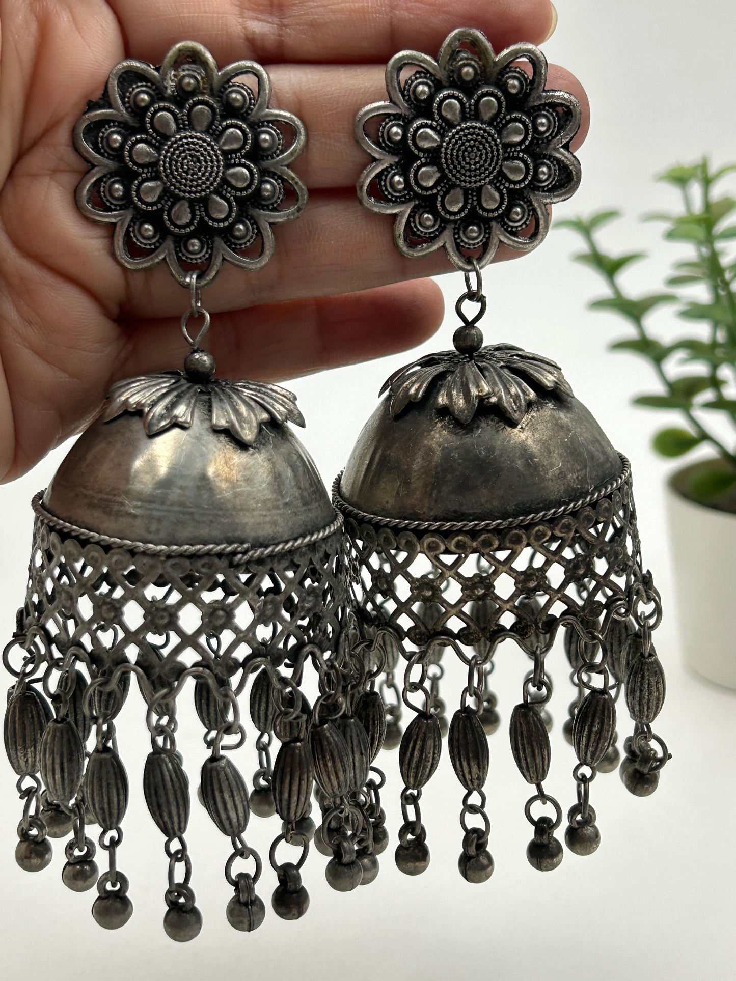 Darsha black polished jhumka earrings shown in hand for size reference, featuring floral stud and dome shape with delicate hanging, bold ethnic statement jewelry