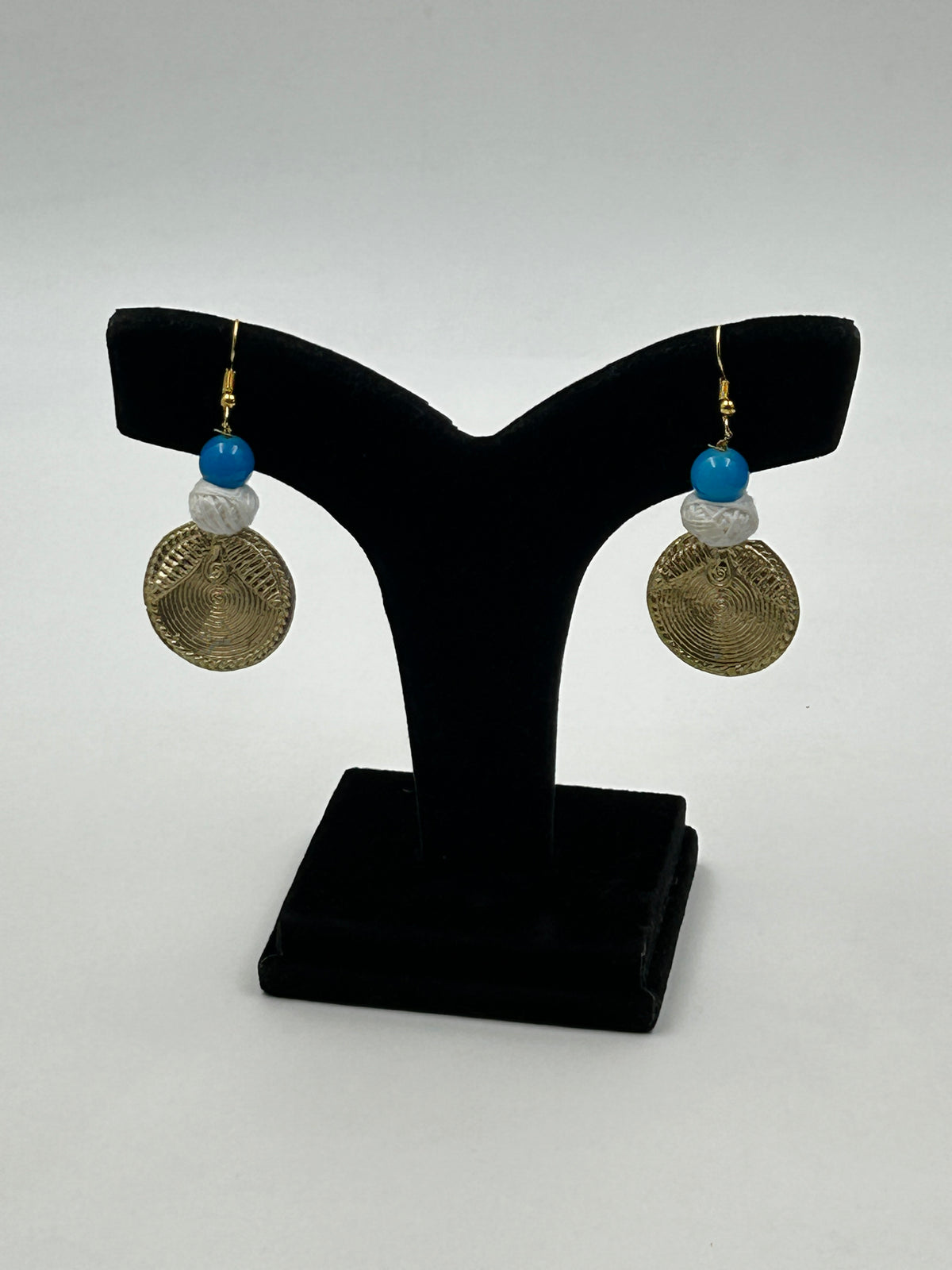 Arohi Blue Dokra handmade matching earrings with brass dokra design, blue bead and white cotton bead on display stand