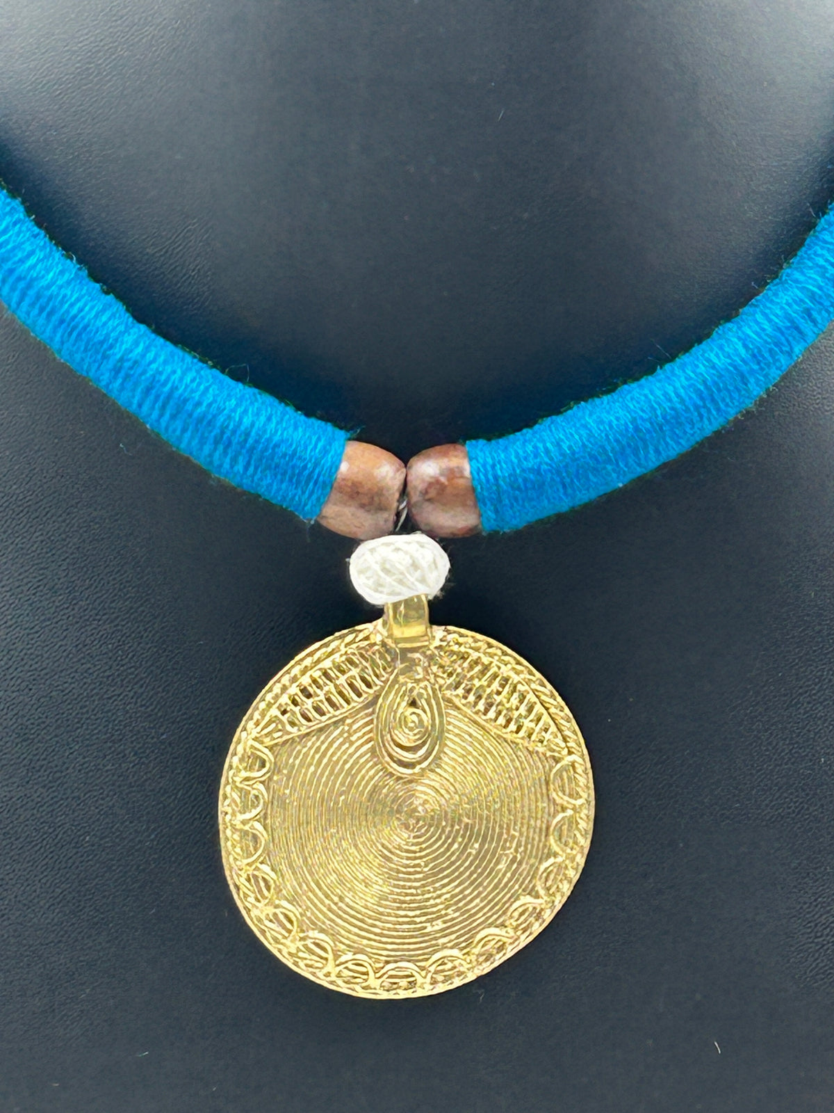 Close-up of Arohi Blue Dokra handmade necklace featuring round brass dokra pendant with spiral design and blue tassel