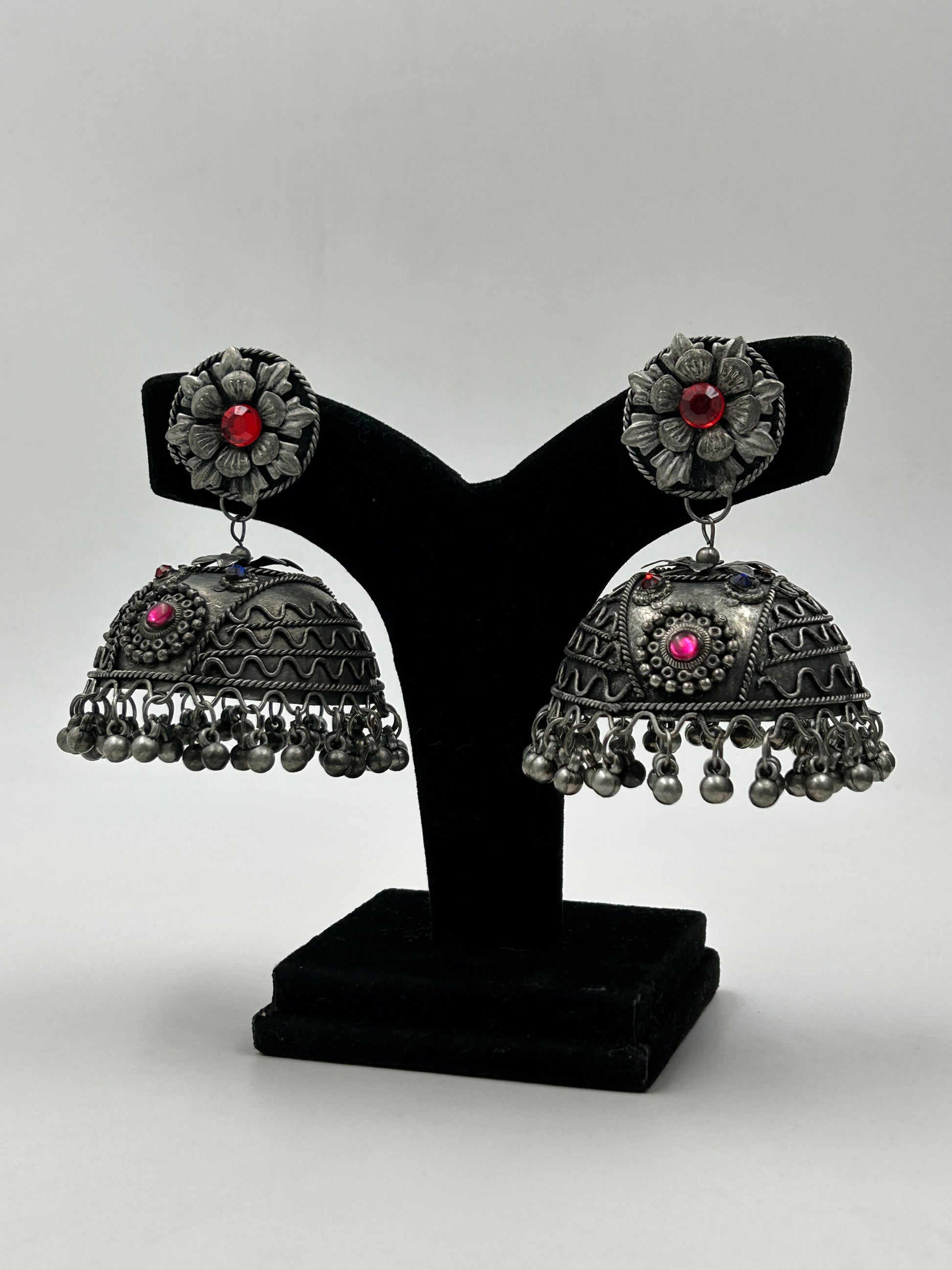 Bhavi black polished jhumka earrings displayed on stand with intricate detailing and silent ghungroo hangings, bold tribal inspired statement earrings for ethnic wear